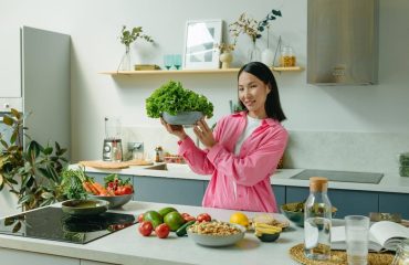 Woman in a kitchen holding fresh lettuce, surrounded by healthy ingredients like tomatoes and avocados, promoting healthy eating.