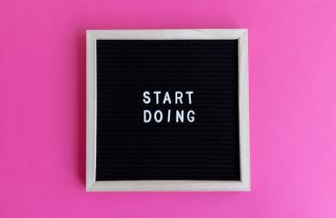 Black letter board with 'Start Doing' motivational text on bright pink background.